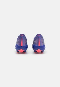 Paarse voetbalschoenen met een gestructureerd ontwerp, voorzien van roze accenten, een achterrits en stervormige noppen op de zool voor grip.