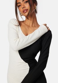 Abito lavorato a maglia bianco e nero con silhouette aderente, maniche lunghe e superficie testurizzata caratterizzata da un distintivo design a blocchi di colore.