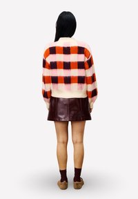 Vrouw met lang donker haar die een roze, rode en bordeaux geruite trui, een donkere leren mini-jurk, bordeaux sokken en een paar bruine instapschoenen draagt.