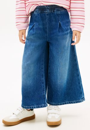 Wide-leg denim trousers in dark blue, featuring an elastic waistband, two front pockets, and a smooth texture. Paired with white sneakers.