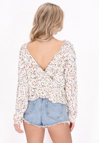 Vit, texturerad tröja med färgglada prickar, med en djup V-rygg och långa ärmar, tillsammans med denimshorts med avskurna ben.