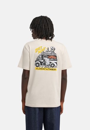 Persona con dreadlocks che indossa una t-shirt beige con un furgoncino dei cartoni animati e il testo "Spilt Paint," "Drips & Splatters," e "Element & Timber" sulla schiena.