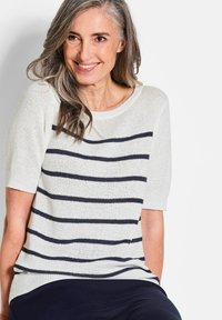 Brede, crèmekleurige gebreide trui met marineblauwe horizontale strepen, met korte mouwen en een brede halslijn, gepresenteerd door een model met lang haar.