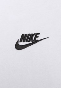 Bílá látka s vyšitým černým logem Nike a zakřiveným designem swoosh, která se vyznačuje čistými liniemi a kontrastními barvami.