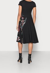 Mustat lyhythihaiset mekko, jossa on värikästä brodeerausta sivuilla, vartalonmyötäinen yläosa ja liehuva hame. Yhdistetty mustiin nilkkureihin.