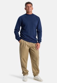 Námořnický svetr s kulatým výstřihem v kombinaci s béžovými skládacími kalhotami a bílými teniskami. Svetr má žebrované manžety a lem. Hladká textilie.