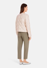 Gepolsterte hellrosa Jacke mit rundem Ausschnitt, mit einem Rautenmuster. Kombiniert mit olivgrünen Hosen und weißen flachen Schuhen.