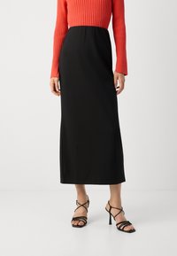 Black, floor-length skirt with a smooth texture, paired with a ribbed red long-sleeve top and black strappy heels.