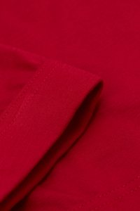 Červená bavlněná tkanina s hladkým povrchem. Tkanina má ohnutý lem s viditelným stehem, což zdůrazňuje její strukturu a design.