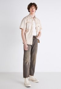 Kortermet beige denimskjorte med sømdetaljer, hvit tank-topp, falmede straight-leg jeans og kremhvite høyde sneakers.