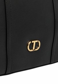Black handbag made of smooth material with gold-tone hardware. Features a prominent logo detail and vertical seam accents.
