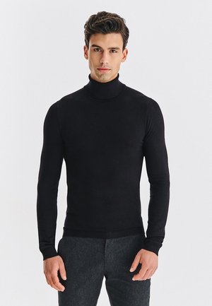 Czarny sweter z golfem z miękkiej tkaniny, o dopasowanym kroju z długimi rękawami i prążkowanym wykończeniem, zestawiony z ciemnymi spodniami.