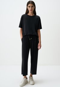 Czarna, oversized t-shirt z krótkimi rękawami w połączeniu z czarnymi spodniami na sznurek. Oba elementy wykonane z gładkiego materiału, a spodnie dodatkowo ozdobione złotymi akcentami.
