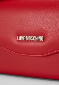 Červená kabelka z umělé kůže s hladkým povrchem, se zlatým logem "LOVE MOSCHINO" a dekorativním prošíváním podél klopy.