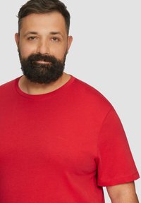 Rode T-shirt met korte mouwen, gemaakt van zachte katoen. Heeft een ronde halslijn en een klein logo in de bovenste linkerhoek. Glad textuur.