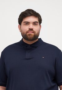 Polo a maniche corte di colore blu navy, realizzato in tessuto morbido, con una patta a due bottoni e un piccolo logo sul lato sinistro del petto.