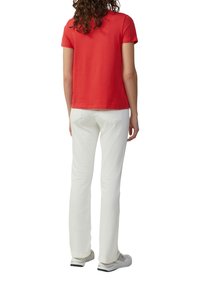 T-shirt rouge à manches courtes, associé à un jean blanc ajusté, vu de l'arrière. Le T-shirt a une texture lisse, les jeans comportent des poches arrière.