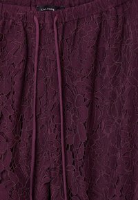 Tessuto in pizzo bordeaux con motivo floreale e superficie testurizzata; presenta una vita elastica e un cordoncino per la regolazione.