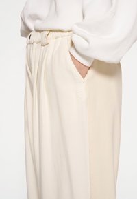Crème-kleurige broek met een relaxte fit, voorzien van een elastische tailleband en zijzakken. De stof heeft een zachte textuur en een subtiele glans.