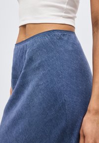 Κοντινό πλάνο ενός ατόμου που φοράει στενή μπλε φούστα και λευκό κοντομάνικο τοπ, δείχνοντας την περιοχή της μέσης και των γοφών.