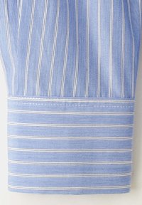 Poignet de chemise bleue avec des fines rayures blanches et bleu foncé verticales sur la manche et des rayures horizontales sur le poignet.