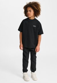 Sort kortærmet t-shirt lavet af blødt stof, kombineret med sorte joggers og hvide højhalsede sneakers med velcro-stropper.