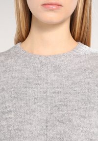 Lichtgrijze wollen trui met een ronde halslijn, voorzien van een zachte textuur en een ribgebreide kraag. Naaddetails zijn zichtbaar aan de voorkant.