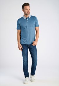 Pikétröja i teal med grå krage, korta ärmar och placket med tre knappar, tillsammans med blå jeans och vita sneakers.