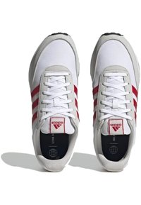 Weiße Sportschuhe mit roten Akzenten und einem Design mit drei Streifen, ausgestattet mit einer strukturierten grauen Sohle und flachen weißen Schnürsenkeln. Minimalistisches Branding.