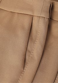 Tissu beige à texture lisse, présentant un design plissé et des coutures visibles le long du bord. Style simple et classique avec une allure ajustée.