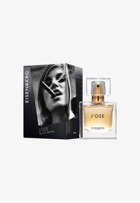 Eisenberg J'ose Eau de Parfum har en klar glasflaska med ett guldfärgat lock, placerad bredvid en svart låda som visar en monokrom bild.