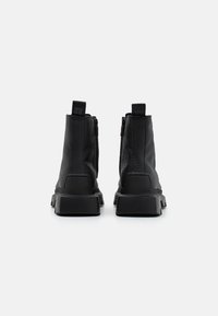 Bottines en cuir noir avec un fini texturé, zips sur les côtés et semelles en caoutchouc épais pour la stabilité. Marquage à l'arrière.