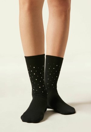 Zwarte geribde sokken met zilveren studs in een stippenpatroon. De boorden zijn elastisch, wat zorgt voor een goede pasvorm.