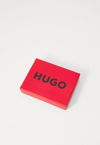 Caja rectangular roja con un acabado suave que presenta la palabra "HUGO" en letras negras en negrita en la superficie superior.