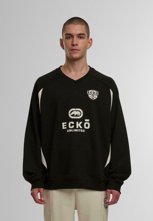 Svart sweatshirt med lange ermer, V-hals og hvite detaljer. Har logoer på brystet og skulderen. Glatt tekstur, bahagelig passform.
