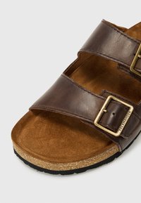 Brune lærsandaler med to justerbare stropper, en suede sål og en korksål. Har bronse-spenner og en teksturert overflate.