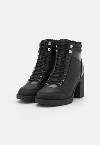 Botas de tobillo negras con tacón, que combinan cuero y ante, con cordones en la parte delantera, ojales plateados y un tacón de bloque texturizado.