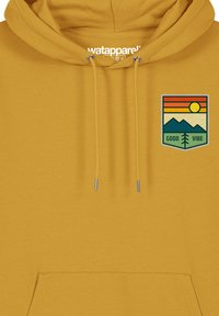 Geel hoodie gemaakt van zachte stof, met een voorzak. Grafische patch bevat een zon, bergen en de tekst "GOOD VIBE" in het groen.