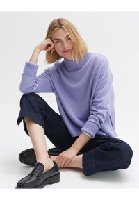 Maglione a maglia di un leggero colore viola con un collo alto, polsini a coste e spacchi laterali. Abbinato a pantaloni scuri e cropped e mocassini neri.