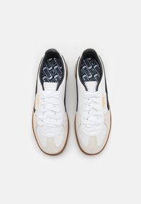 Białe i beżowe sneakersy z czarnymi akcentami, z teksturowaną cholewką, sznurowadłami i gumową podeszwą. Wnętrze ma wzorzystą wkładkę.