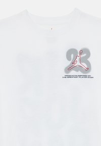 Camiseta blanca de algodón con un diseño gráfico en gris y rojo del número 23 y una silueta de una figura saltando en la parte frontal.