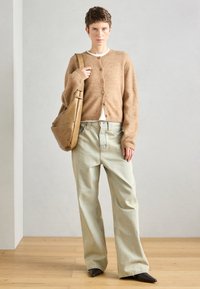 Καφέ, μαλακό πουλόβερ με κουμπιά, συνδυασμένο με ανοιχτόχρωμα τζιν με φαρδιά πόδια και καφέ γόβες. Ολοκληρώνεται με μια μπεζ τσάντα ώμου.