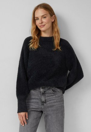 Donker gebreide trui met een gestructureerde afwerking, ronde hals en brede mouwen, gecombineerd met grijze, nauwsluitende jeans. Soepele stof, casual ontwerp.