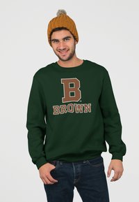 Felpa verde scuro con una grande "B" marrone e la scritta "BROWN". Indossata con un berretto lavorato a maglia giallo senape con un pompon in cima.