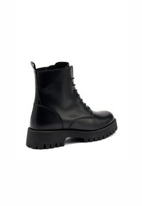 Botas de tobillo de cuero negro con cordones, suela de goma gruesa, parte superior texturizada, tirador y puntera redondeada. Presentan un acabado suave y un diseño resistente.