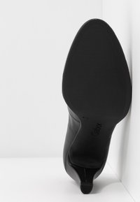 Semelle d'une chaussure à talon en cuir noir reposant contre un coin blanc, montrant une adhérence texturée et la marque "Gabor" en taille 4,5.