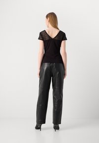 Top noir ajusté avec des détails en dentelle aux épaules, décolleté en V, associé à un pantalon en cuir noir ample, avec une texture lisse et soyeuse.