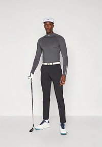 Golfo apranga, kurios sudėtyje yra aptemptas pilkos spalvos ilgos rankovės viršus, juodos kelnės, baltas diržas ir balti batai su mėlynais akcentais, derinami su balta kepure.