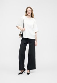 Νεαρή γυναίκα που φοράει ένα λευκό φαρδύ μπλουζάκι, μαύρο παντελόνι με φαρδιά πόδια, μαύρα ψηλοτάκουνα και μια μικρή τσάντα χιαστί με animal print.