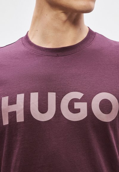 Лилава памучна тениска с голямо светло "HUGO" лого отпред, кръгло деколте и къси ръкави. Гладка текстура.